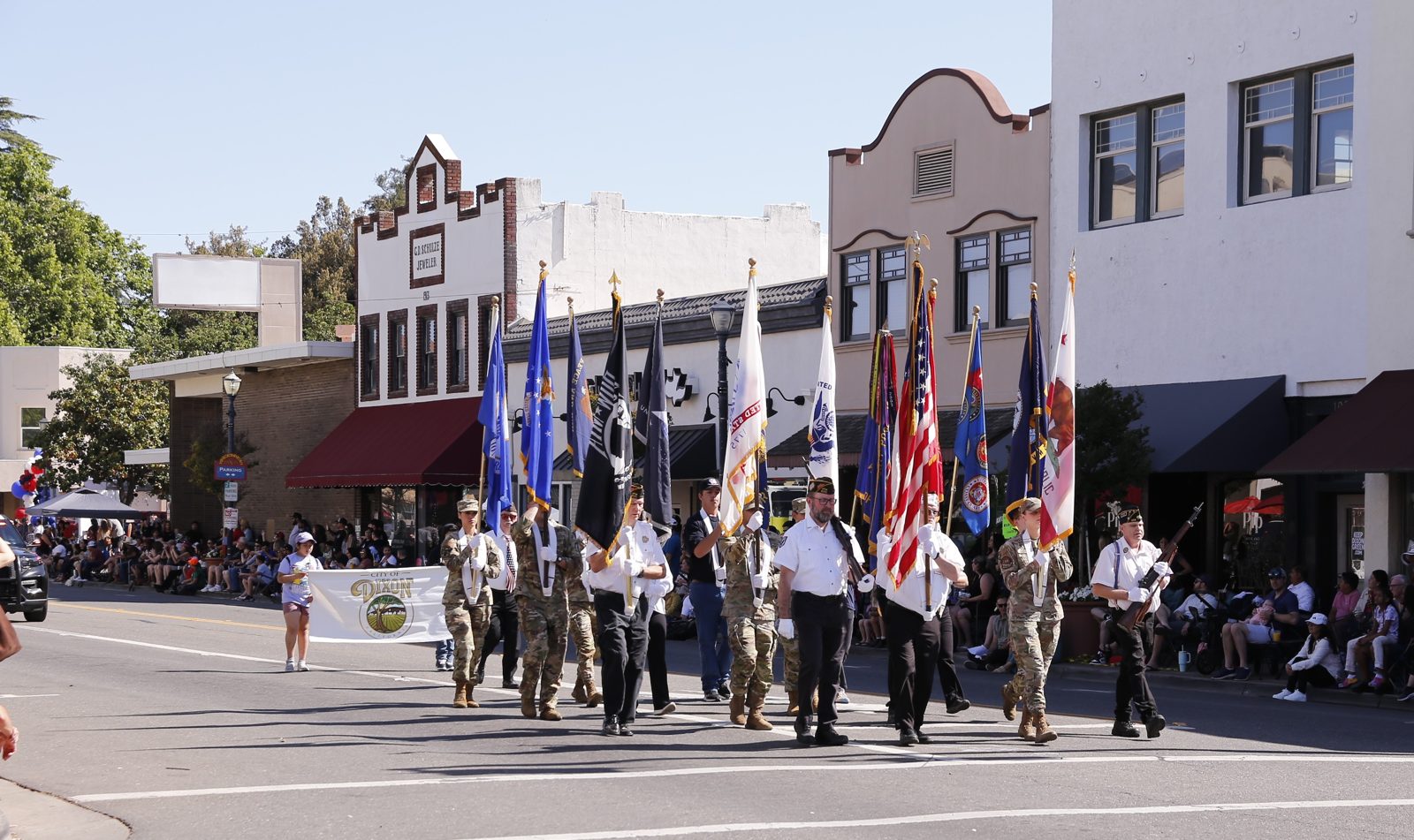 Veterans color guard carrying flags down First Street past historic downtown storefronts